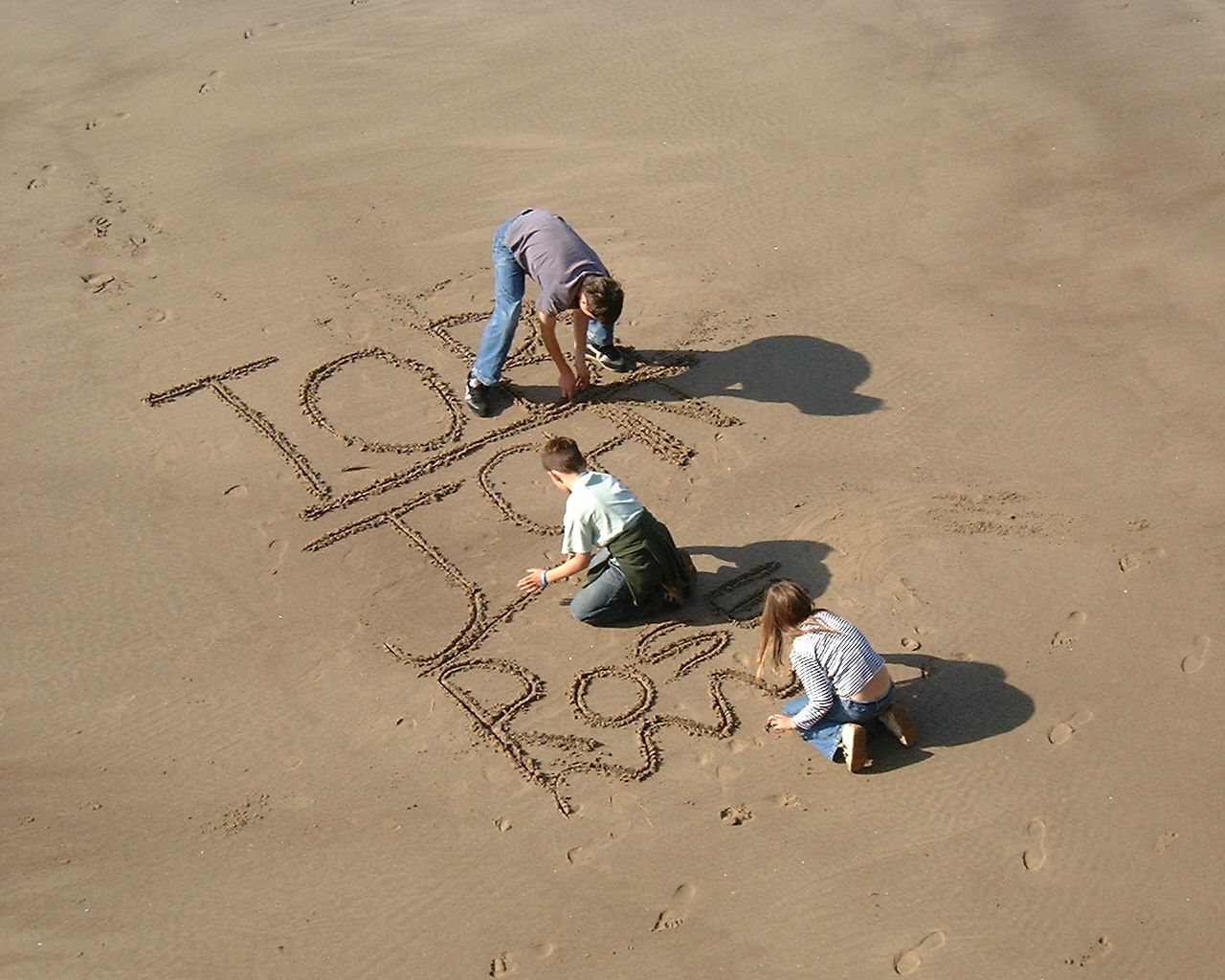 Toby, John and Rose writing their names in the sand. On the beach in Whitby, taken from above. It's a glorious sunny day.